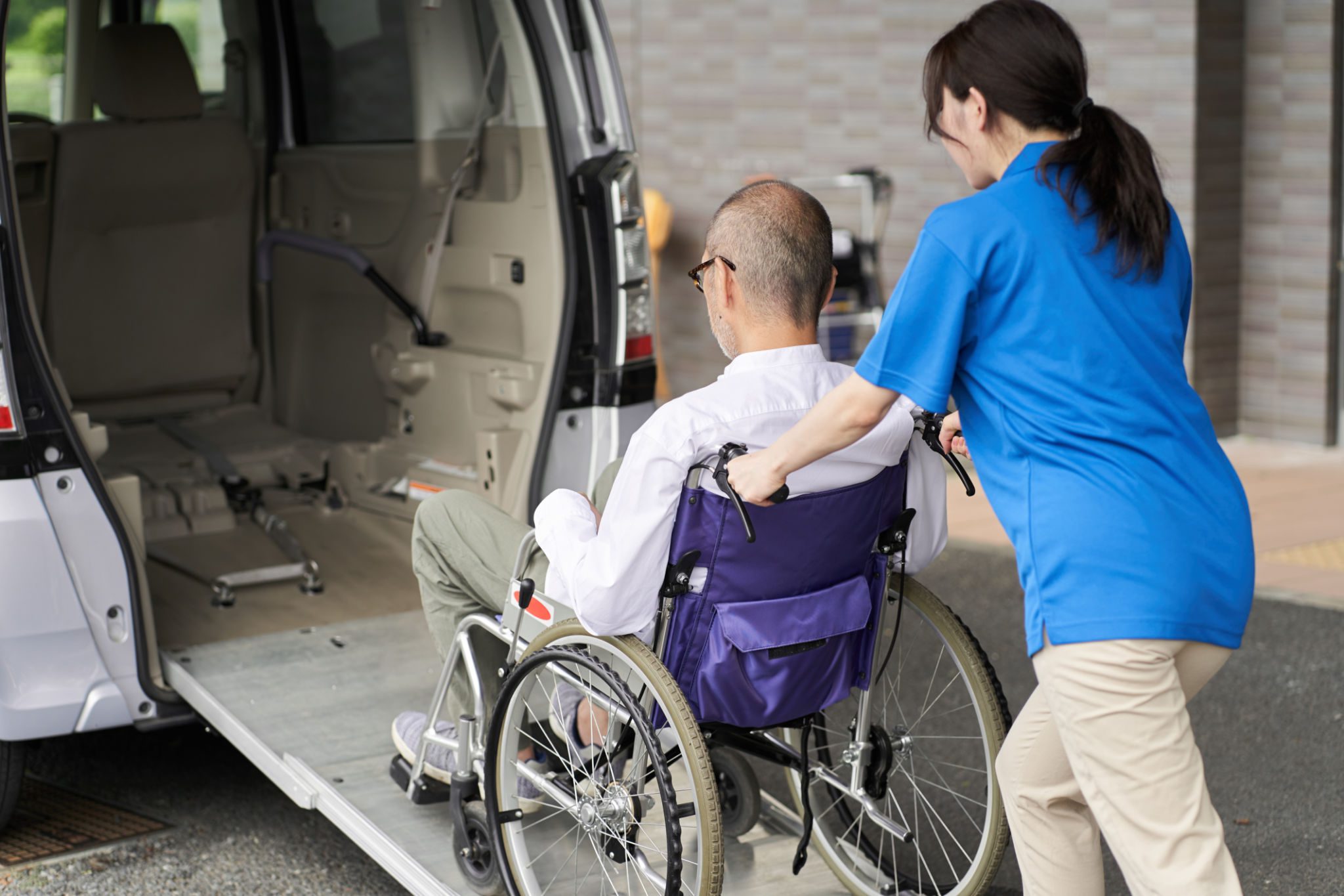 Caregiver assisting man in wheelchair into van.